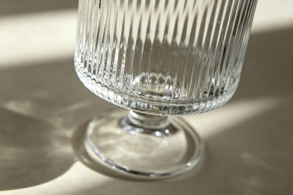 Close-up shot of vertical ribbed stemmed clear glass cup with sunlight shadow texture