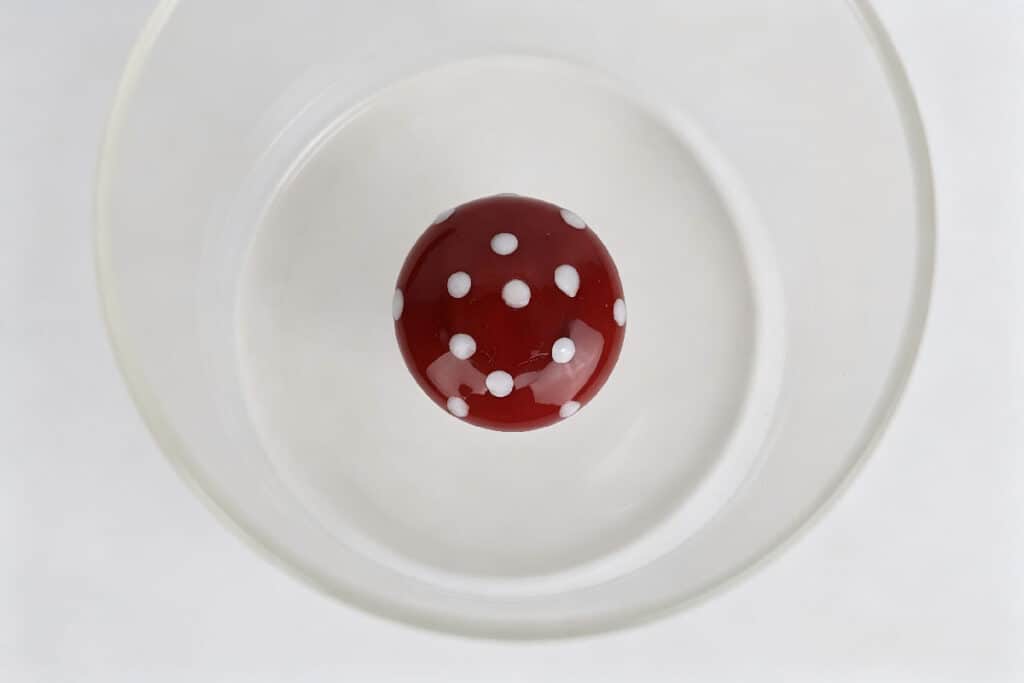 Top-down view of red white polka dot mushroom ornament inside clear glass tumbler