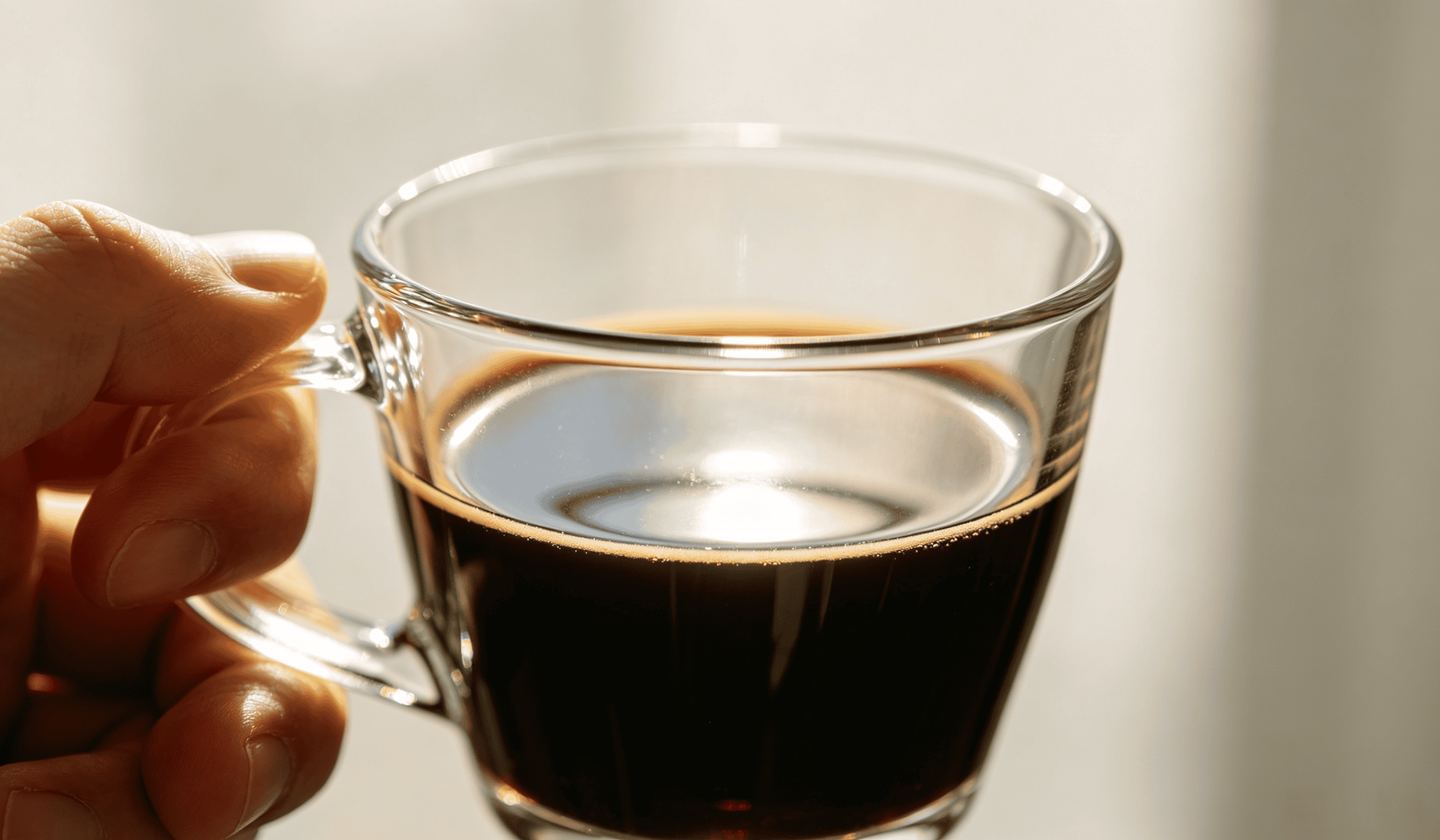 Hand holding a clear glass coffee cup with handle, filled with black coffee