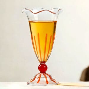 Handblown transparent stemmed glass cup with wavy rim, orange stripe decoration, filled with golden beverage, for dessert, cocktail and milkshake