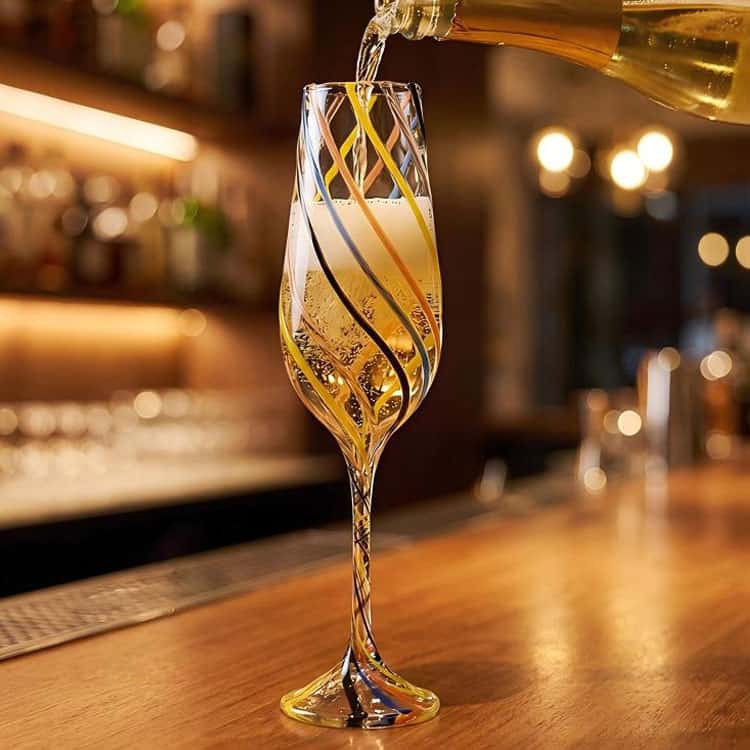Handblown multicolor swirl striped champagne flute on bar counter, pouring sparkling wine into the glass, bar scene photography