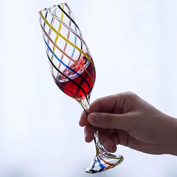 Handheld handblown wine goblet with multicolor twisted swirl stripes, filled with red wine, handmade artistic stem glass