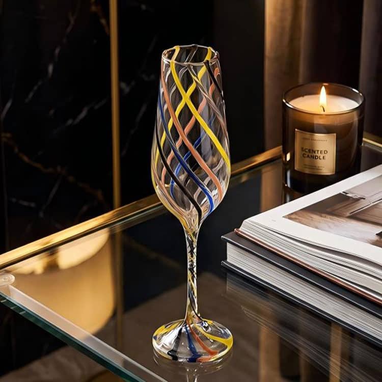 Handblown color swirl striped champagne flute displayed on luxury glass table, elegant home decor scene with candle and books